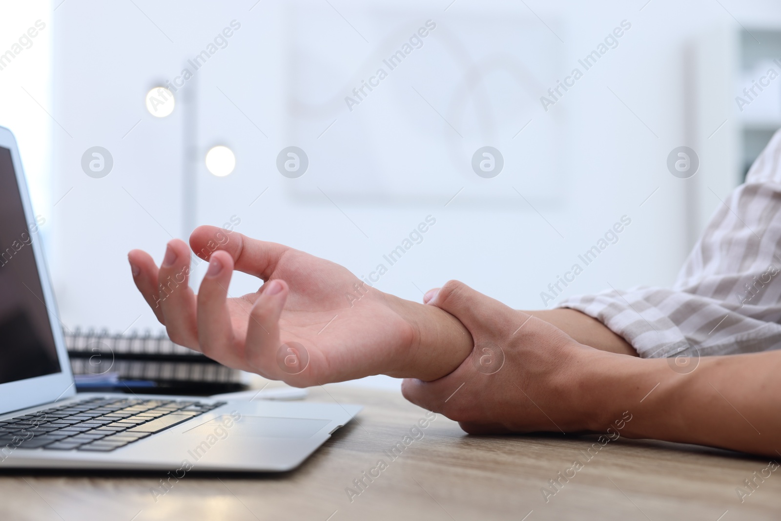 Photo of Man suffering from pain in wrist while working on laptop at table indoors, closeup. Carpal tunnel syndrome