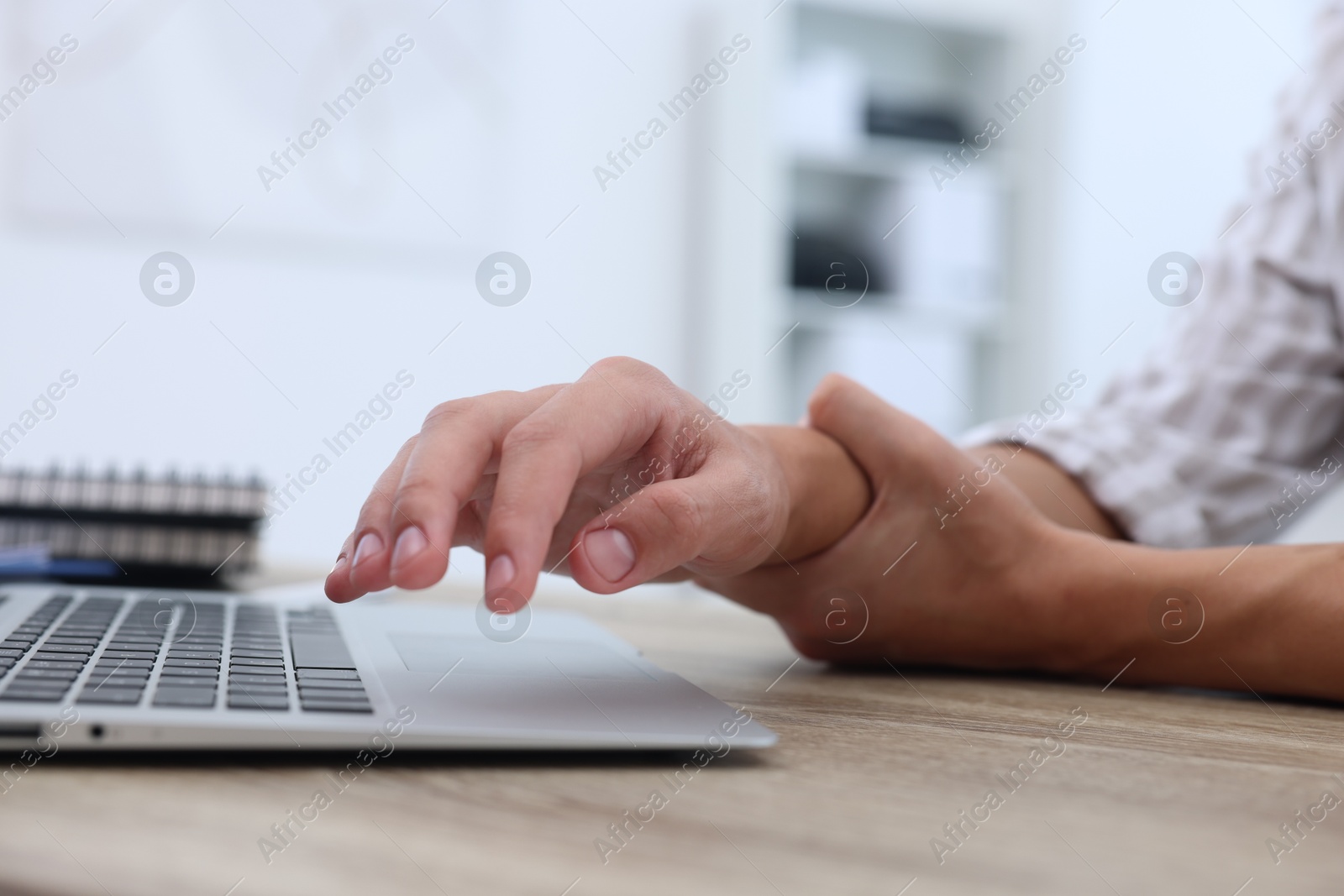 Photo of Man suffering from pain in wrist while working on laptop at table indoors, closeup. Carpal tunnel syndrome