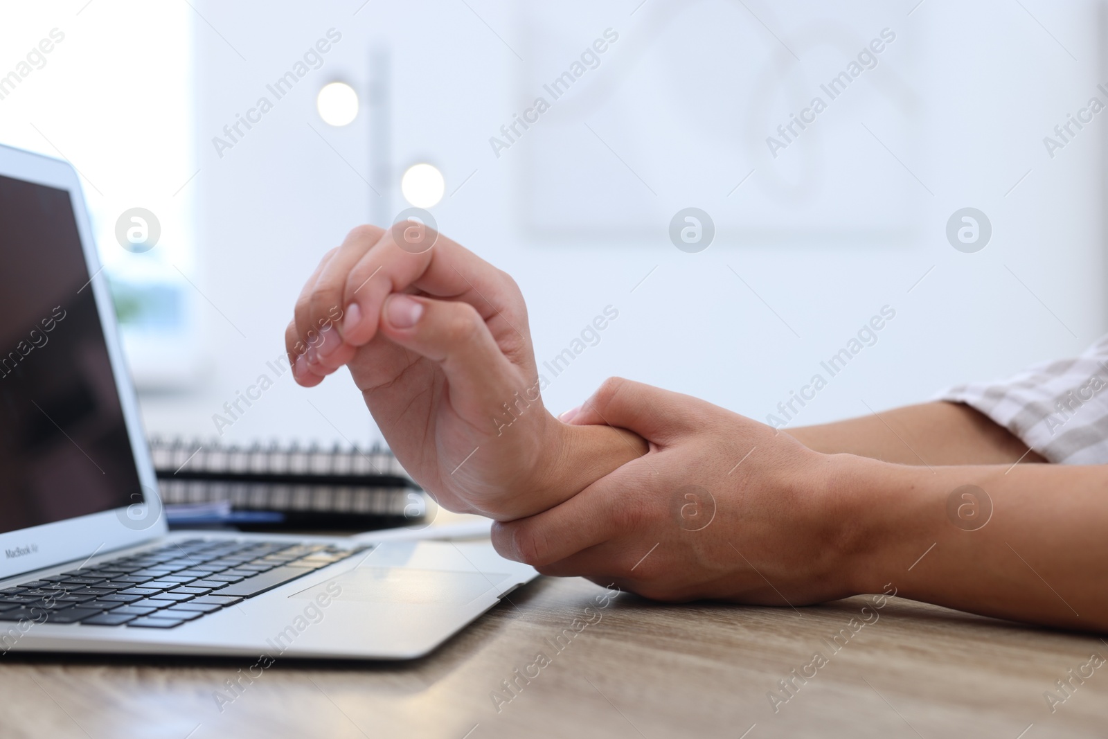 Photo of Man suffering from pain in wrist while working on laptop at table indoors, closeup. Carpal tunnel syndrome