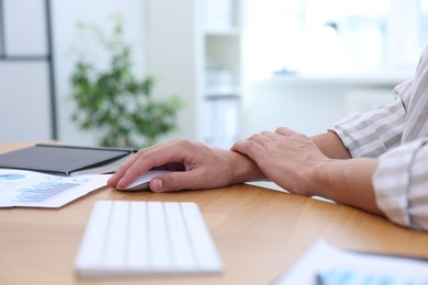 Photo of Man suffering from pain in wrist while using computer mouse at table indoors, closeup. Carpal tunnel syndrome