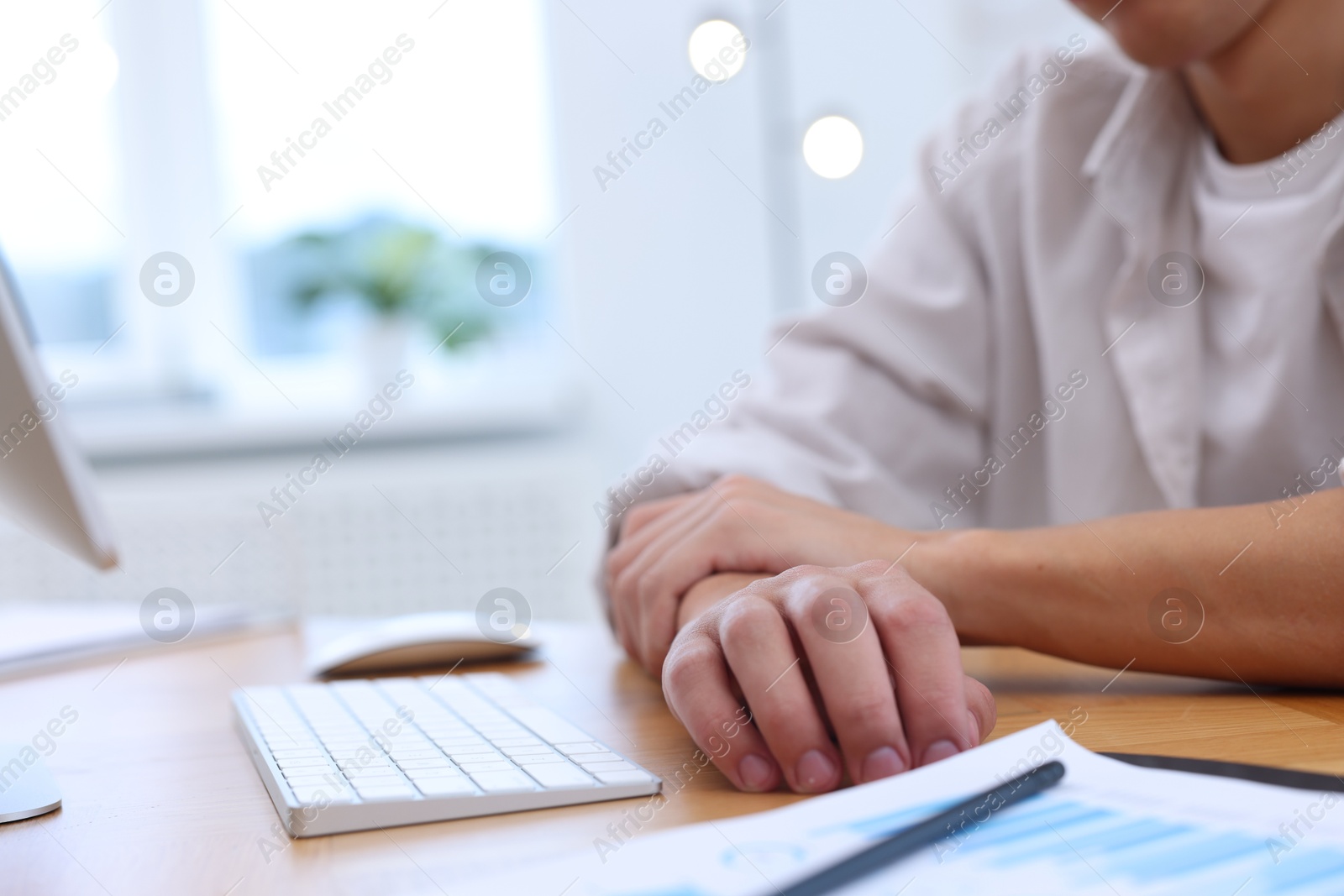 Photo of Man suffering from pain in wrist while working on computer at table indoors, closeup. Carpal tunnel syndrome