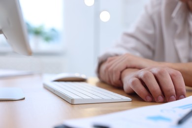 Photo of Man suffering from pain in wrist while working on computer at table indoors, closeup. Carpal tunnel syndrome