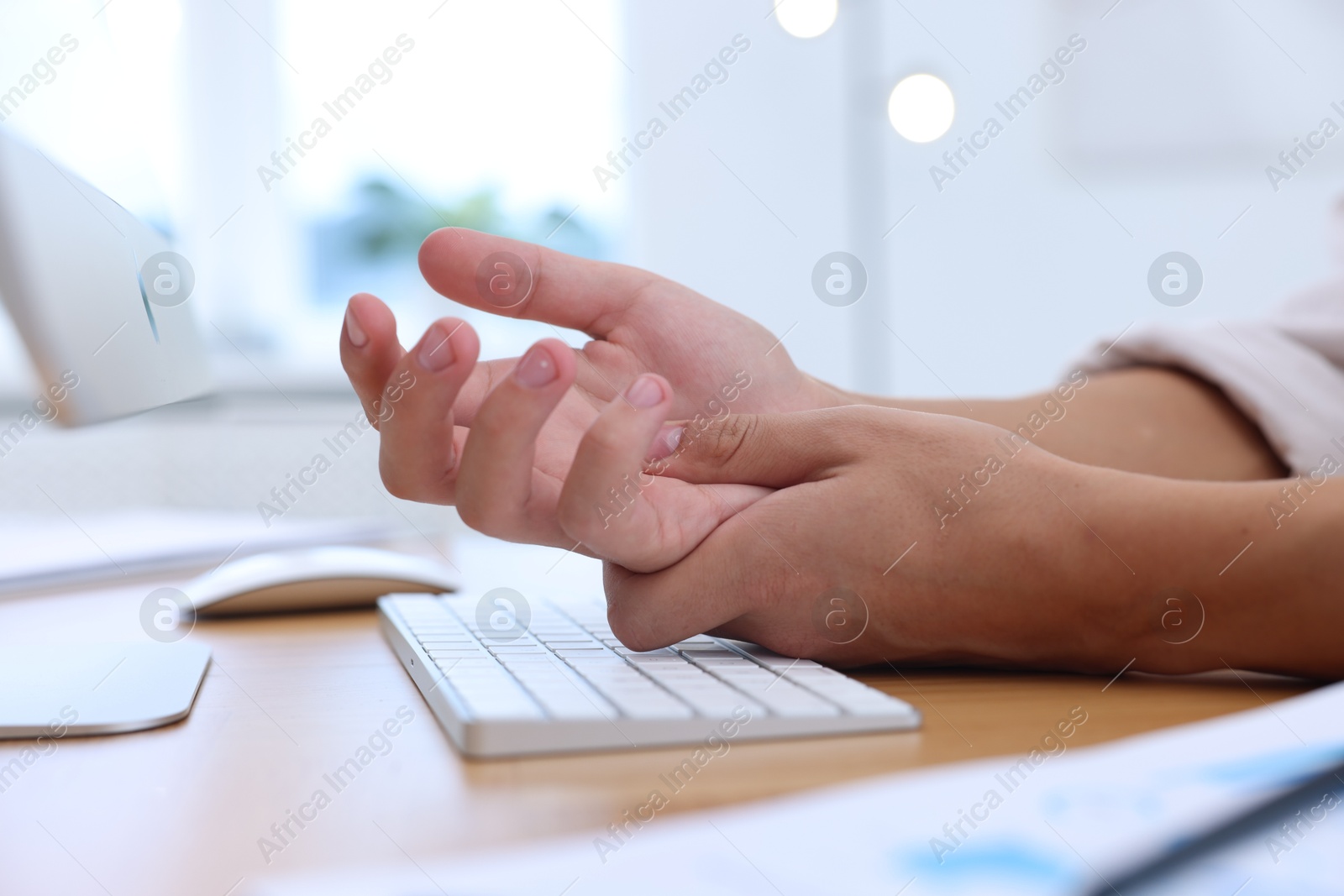 Photo of Man suffering from pain in wrist while working on computer at table indoors, closeup. Carpal tunnel syndrome