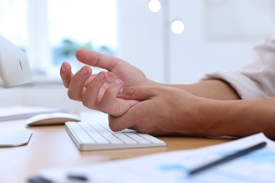 Photo of Man suffering from pain in wrist while working on computer at table indoors, closeup. Carpal tunnel syndrome