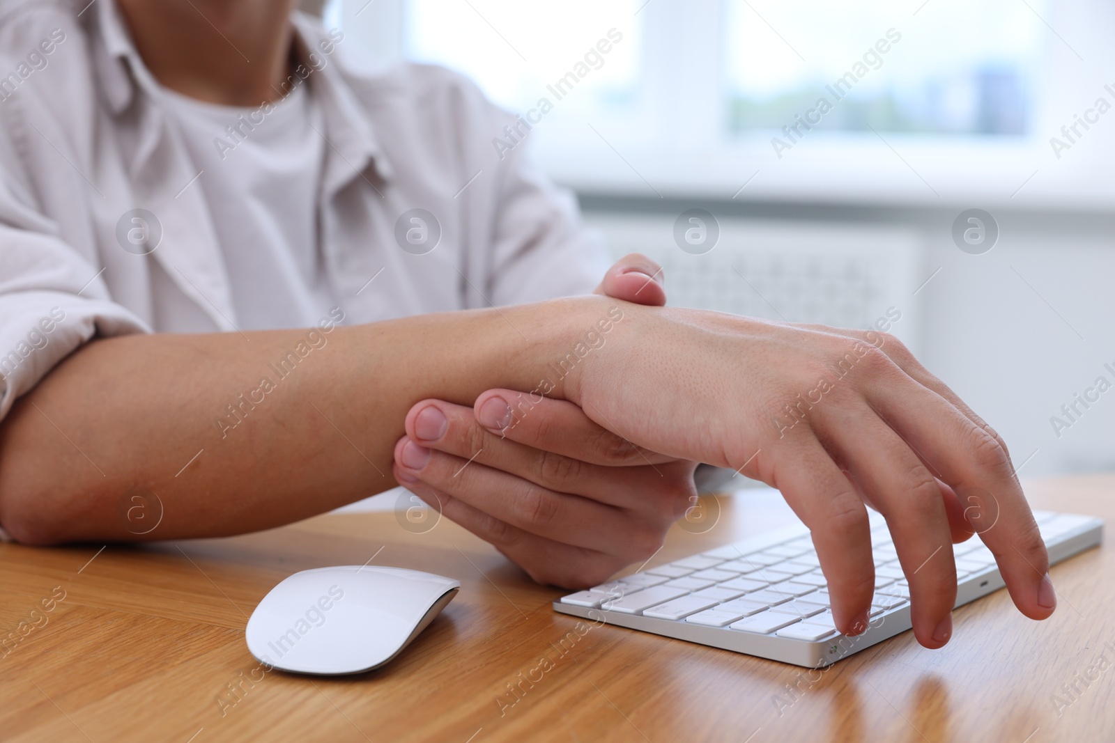 Photo of Man suffering from pain in wrist while working on computer at table indoors, closeup. Carpal tunnel syndrome