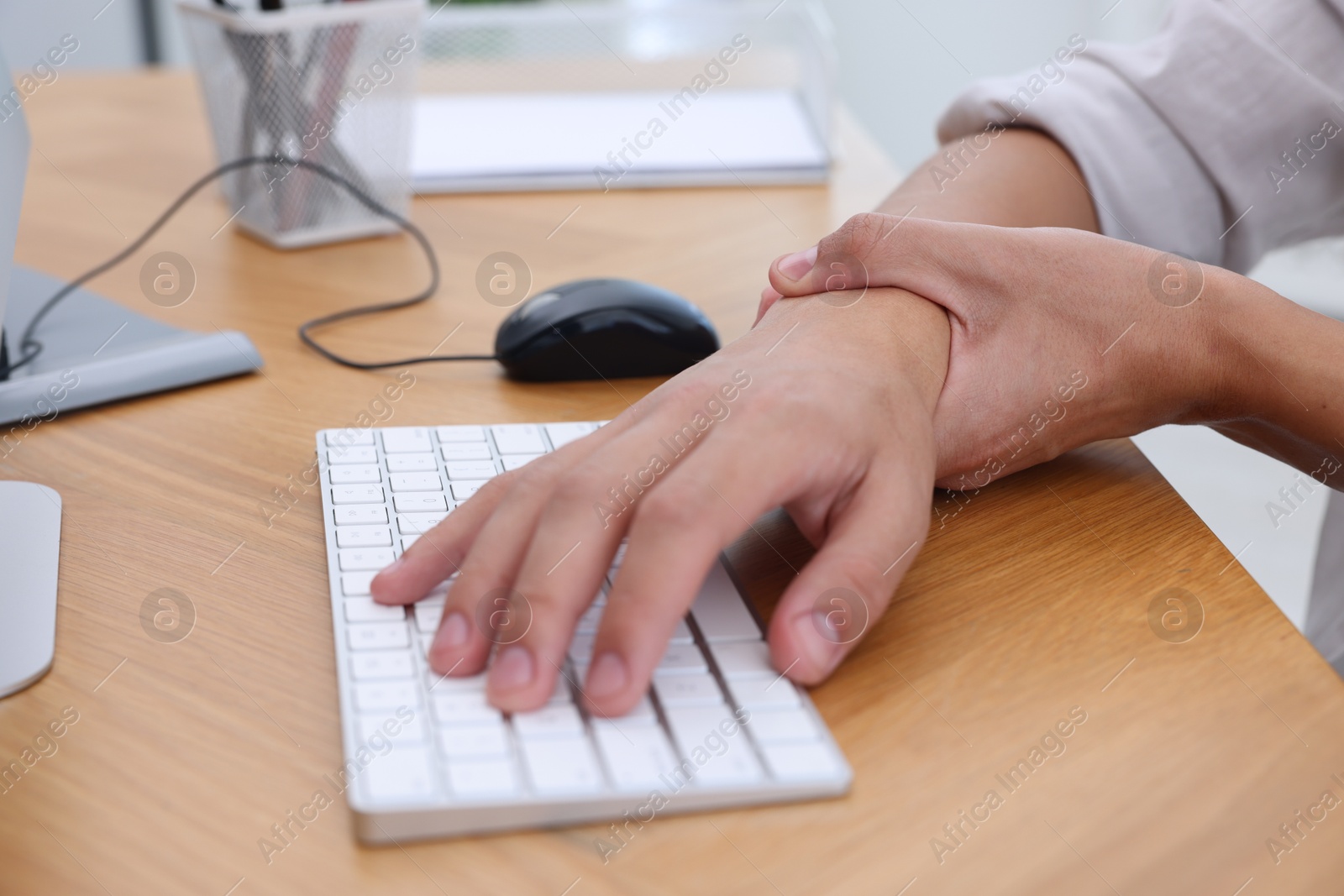 Photo of Man suffering from pain in wrist while working on computer at table indoors, closeup. Carpal tunnel syndrome