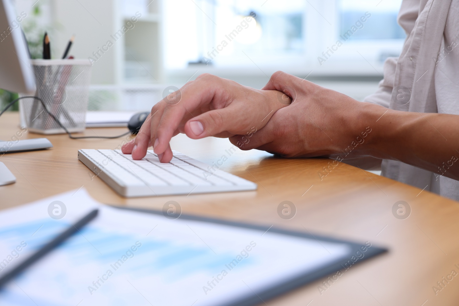 Photo of Man suffering from pain in wrist while working on computer at table indoors, closeup. Carpal tunnel syndrome