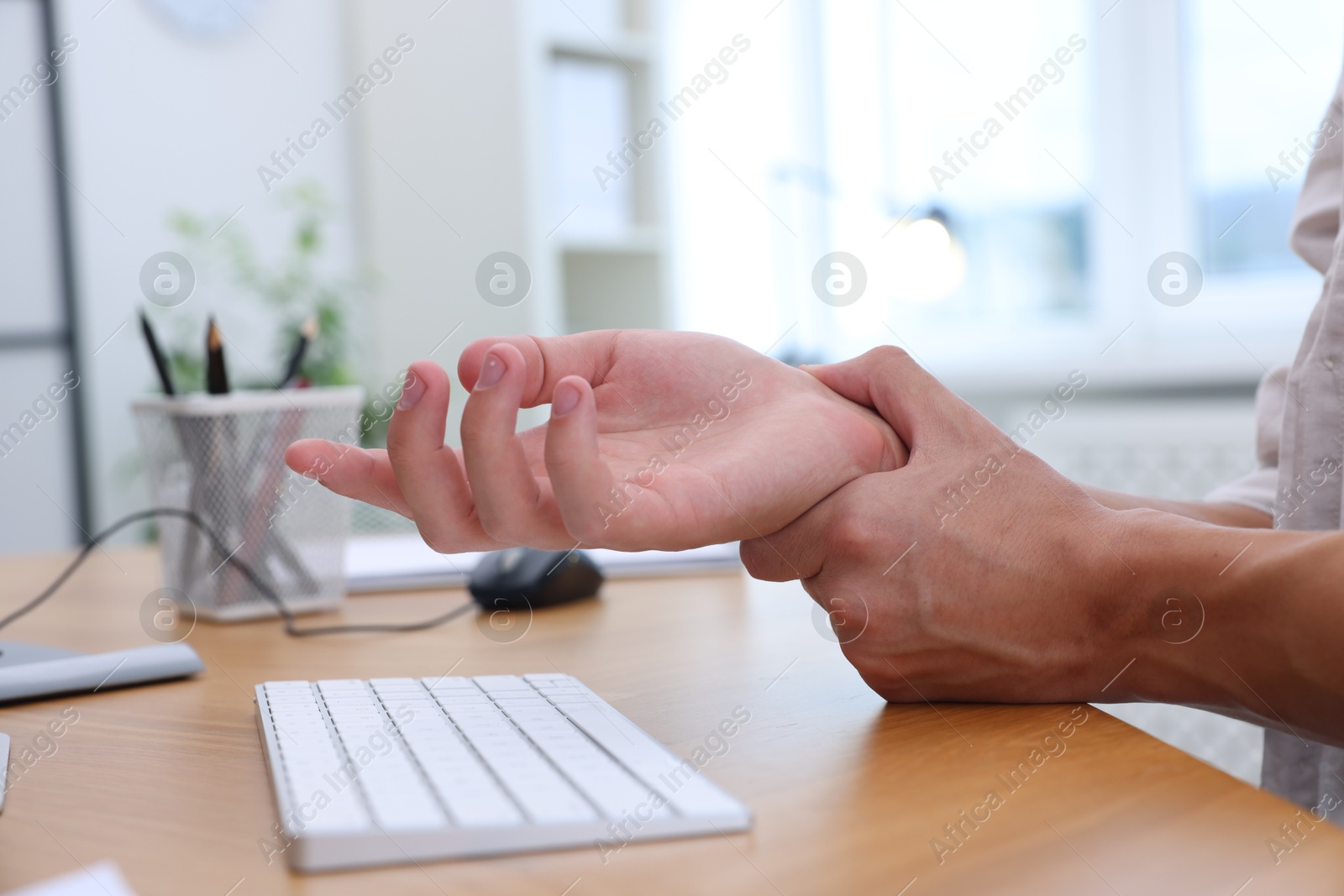 Photo of Man suffering from pain in wrist while working on computer at table indoors, closeup. Carpal tunnel syndrome