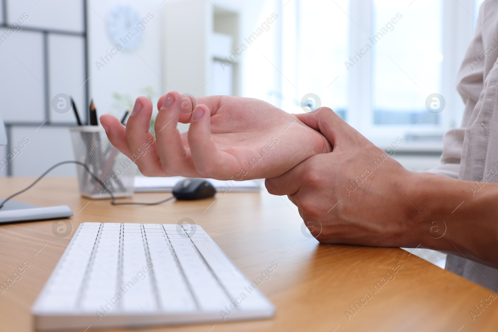 Photo of Man suffering from pain in wrist while working on computer at table indoors, closeup. Carpal tunnel syndrome