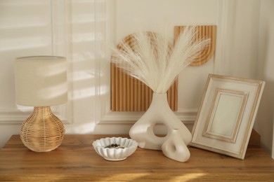 Beautiful decorative plants, vases, photo frame, ceramic bowl and lamp on wooden table indoors