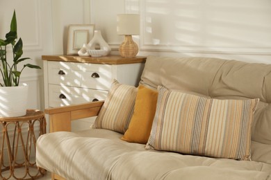 Photo of Sofa with soft pillows, chest of drawers, different decorative elements and houseplant indoors