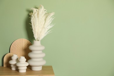 Photo of Beautiful decorative plants, vases and wooden boards on table near green wall indoors, space for text