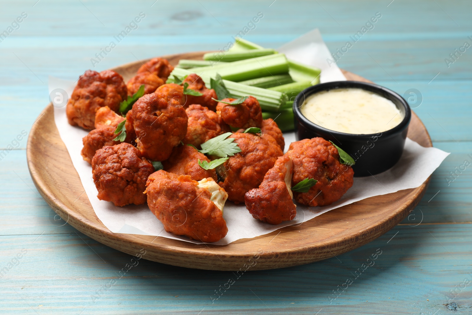 Photo of Baked cauliflower buffalo wings with celery and sauce on light blue wooden table, closeup