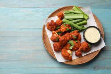 Photo of Baked cauliflower buffalo wings with celery and sauce on light blue wooden table, top view. Space for text