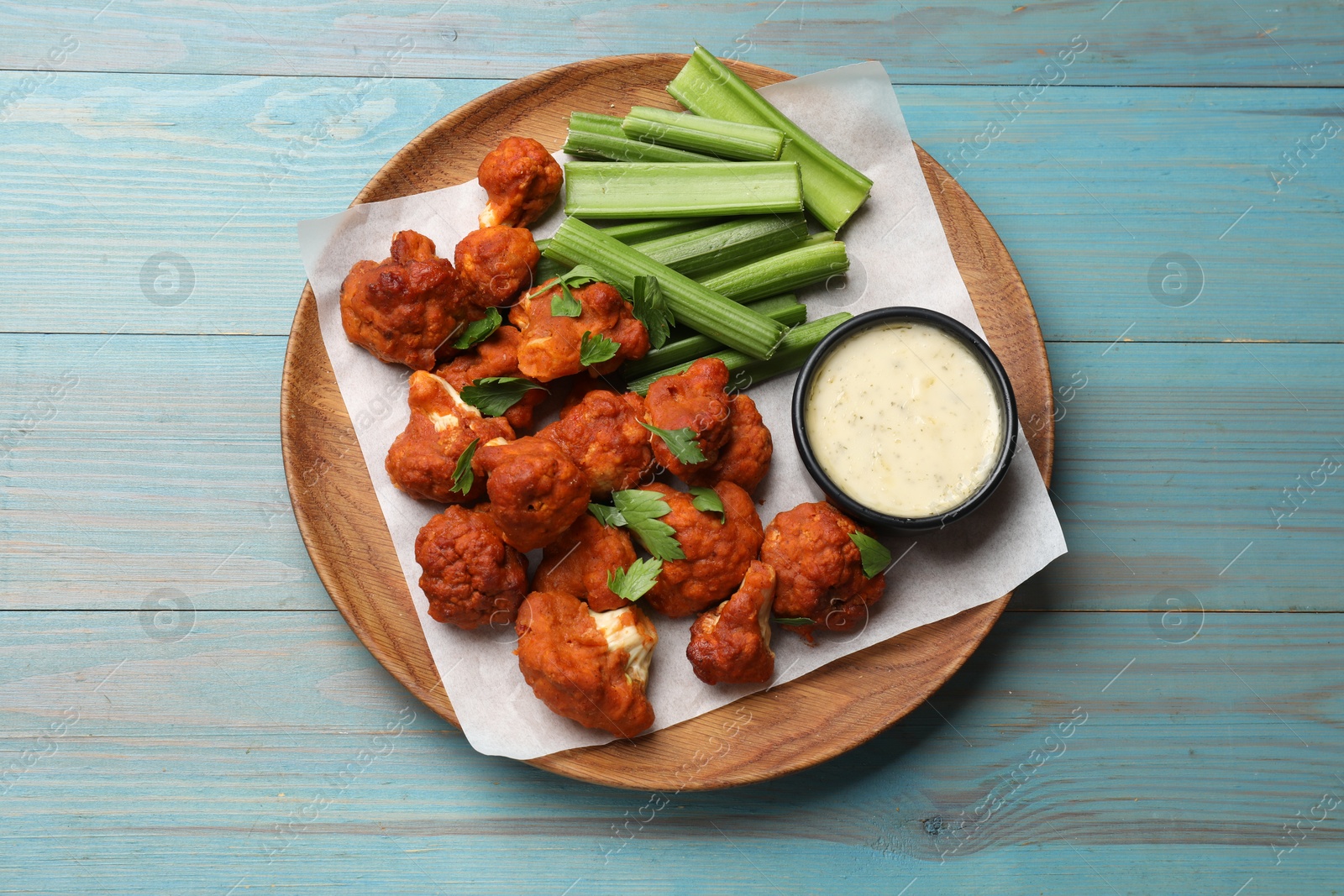 Photo of Baked cauliflower buffalo wings with celery and sauce on light blue wooden table, top view