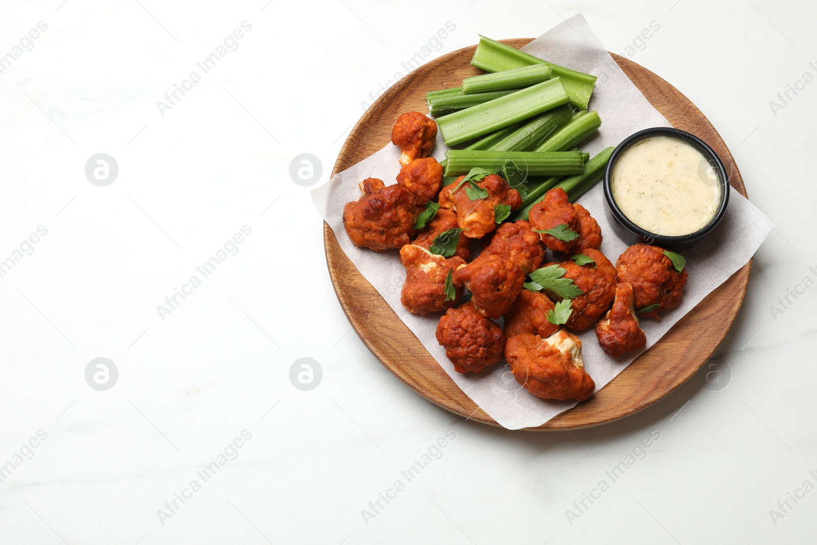 Photo of Baked cauliflower buffalo wings with celery and sauce on white table, top view. Space for text