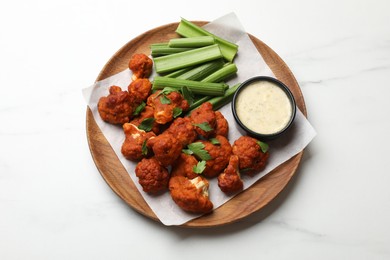 Photo of Baked cauliflower buffalo wings with celery and sauce on white marble table, top view