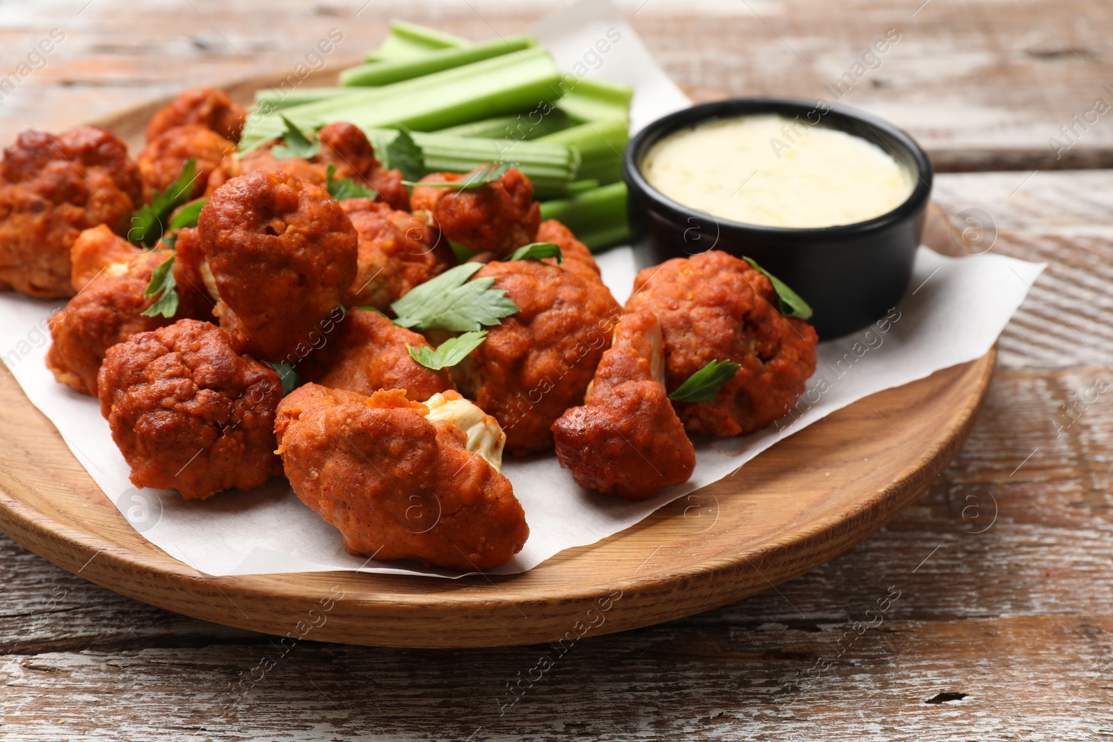 Photo of Baked cauliflower buffalo wings with celery and sauce on wooden table, closeup