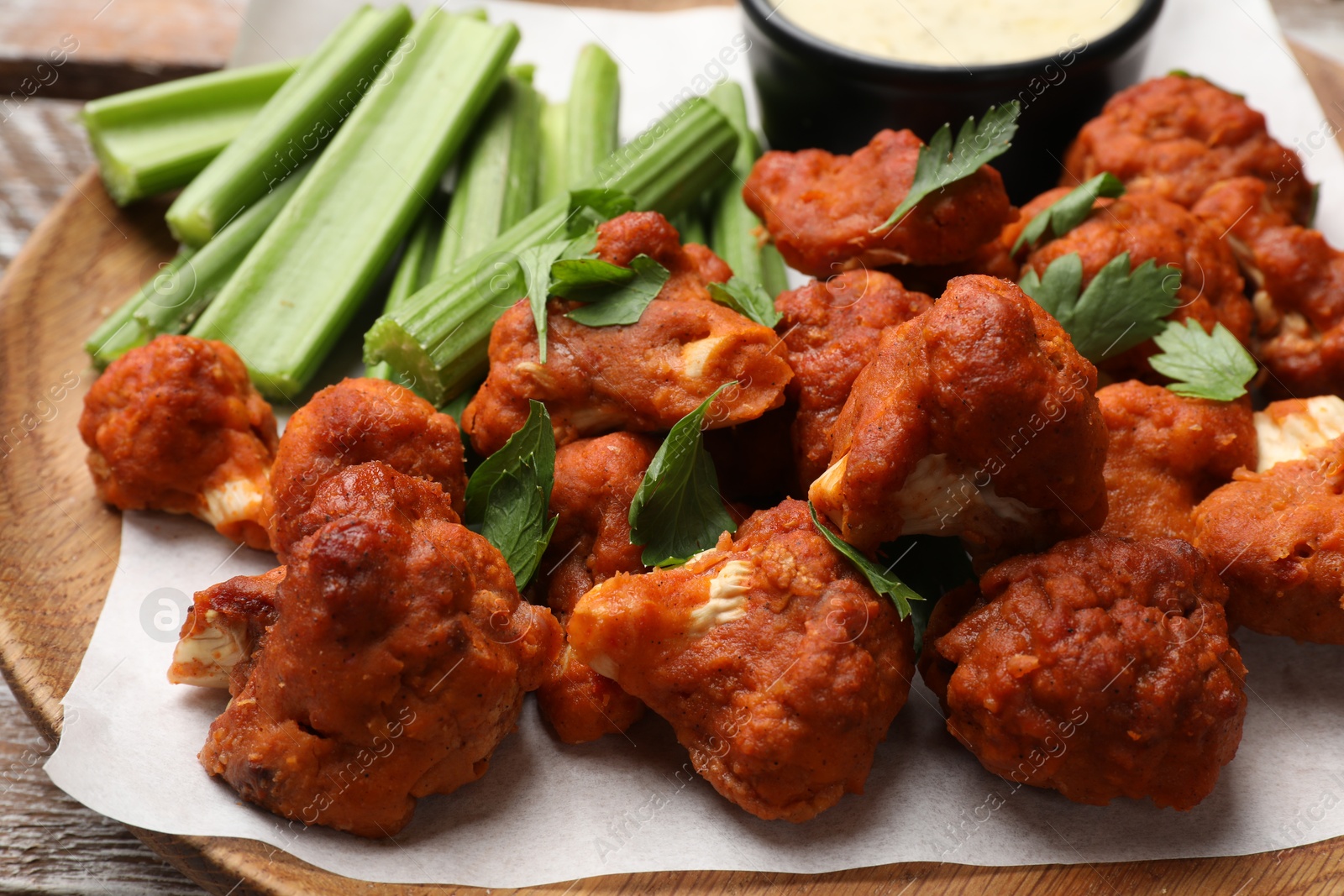 Photo of Baked cauliflower buffalo wings with celery and sauce on table, closeup