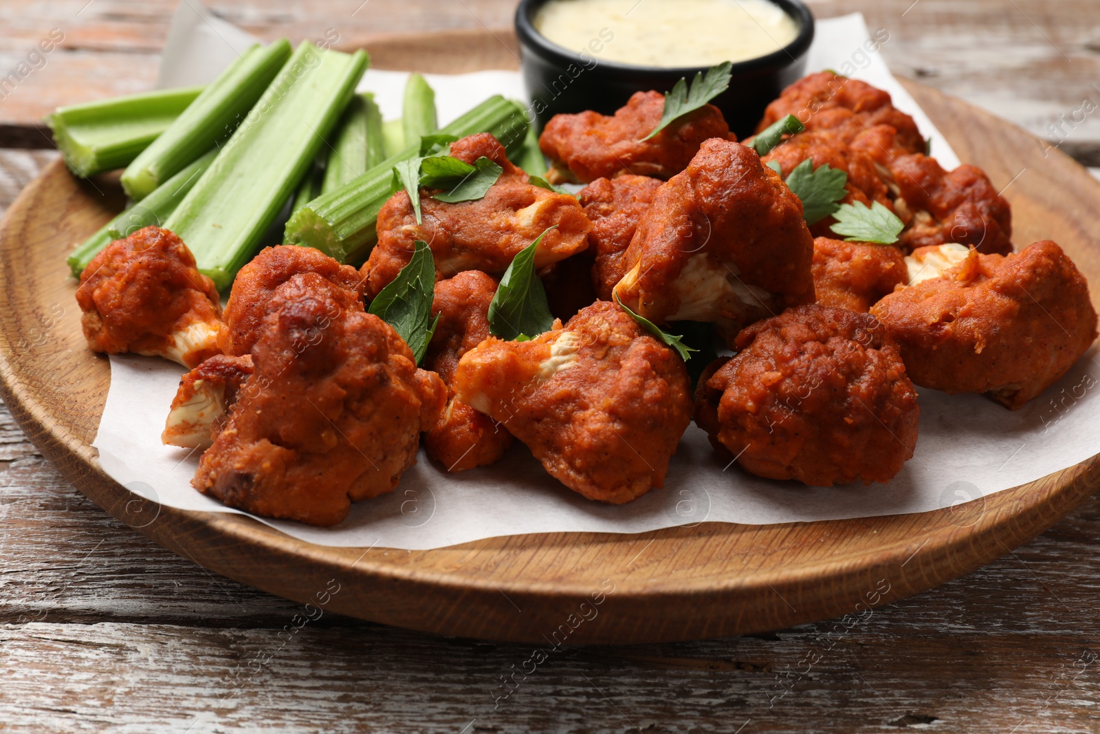 Photo of Baked cauliflower buffalo wings with celery and sauce on wooden table, closeup