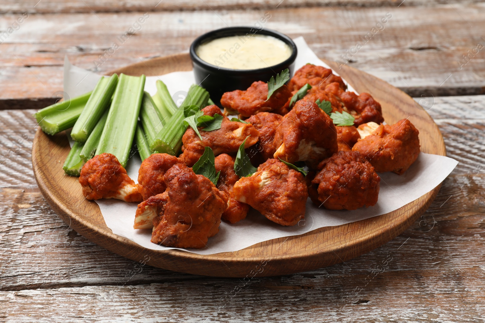 Photo of Baked cauliflower buffalo wings with celery and sauce on wooden table, closeup