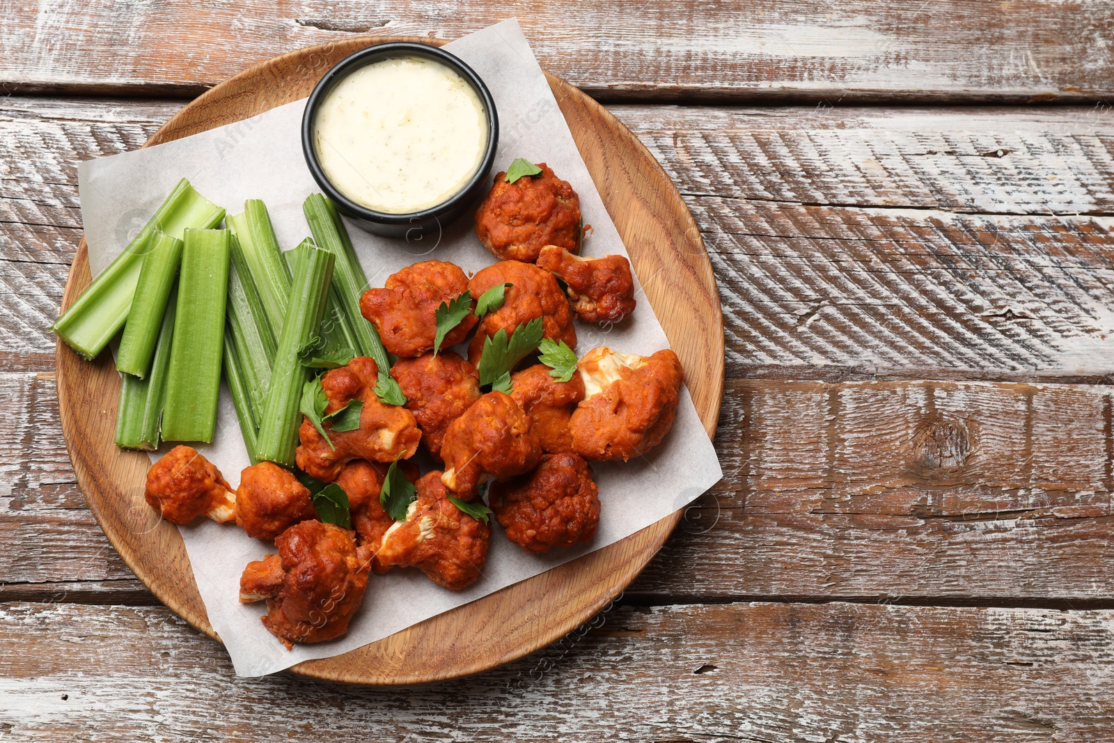 Photo of Baked cauliflower buffalo wings with celery and sauce on wooden table, top view. Space for text