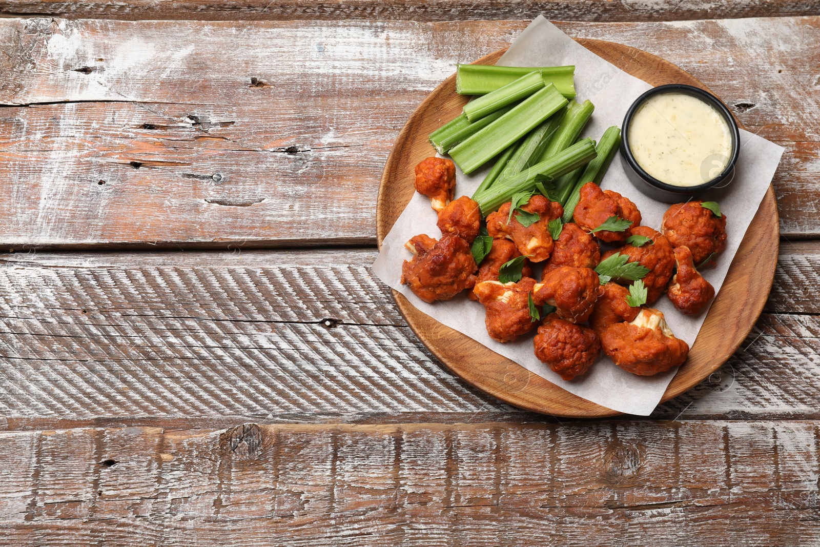 Photo of Baked cauliflower buffalo wings with celery and sauce on wooden table, top view. Space for text