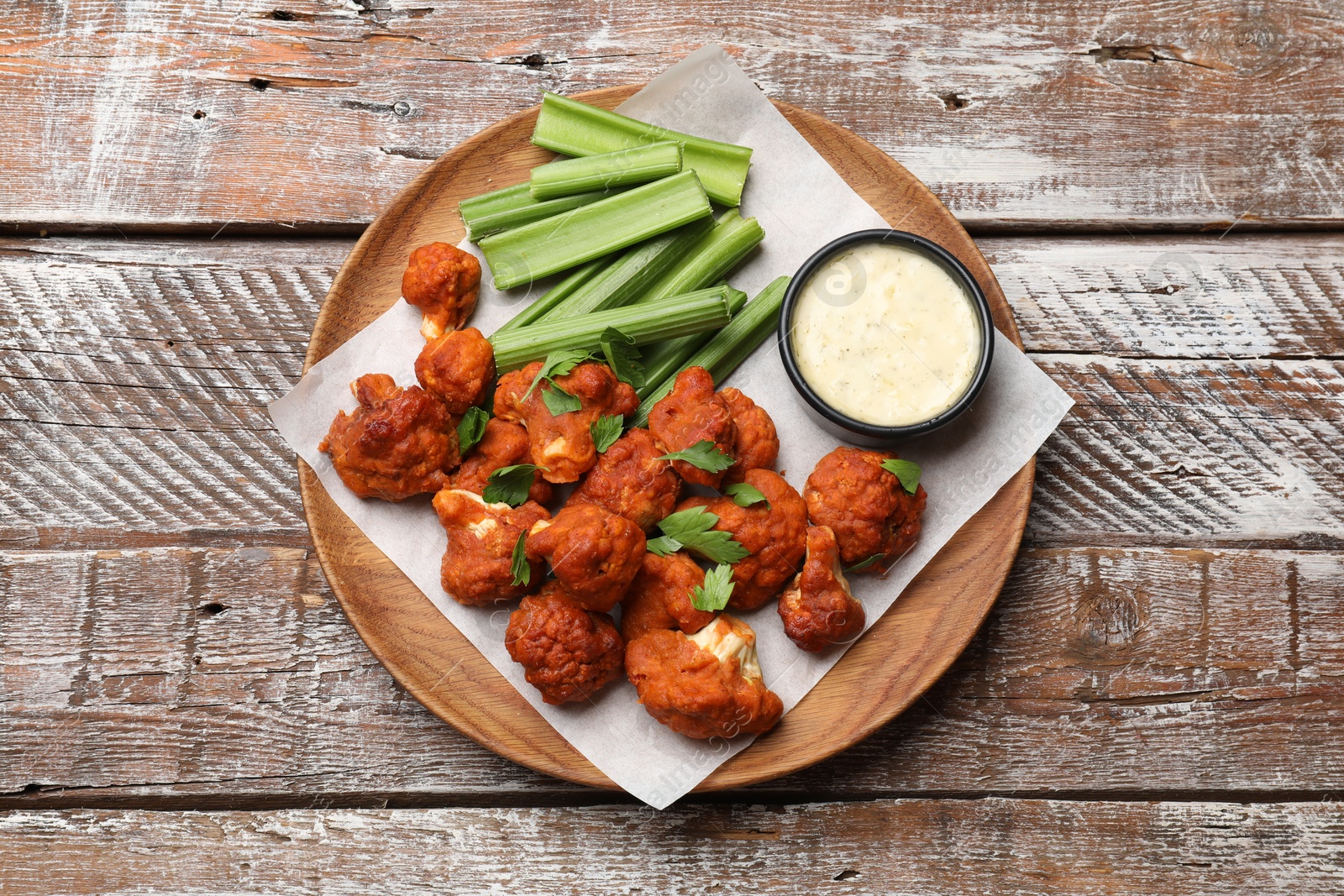 Photo of Baked cauliflower buffalo wings with celery and sauce on wooden table, top view