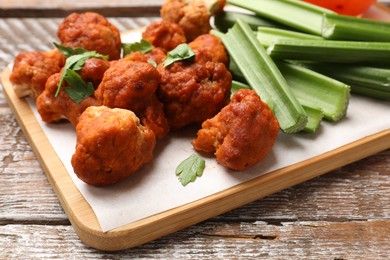 Photo of Baked cauliflower buffalo wings with parsley and celery on wooden table, closeup