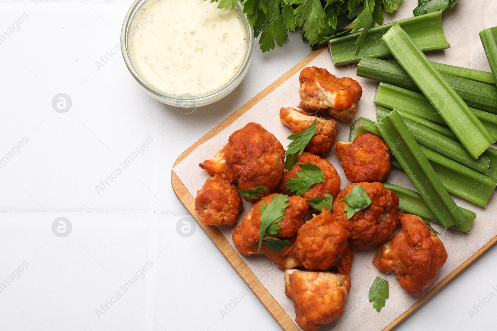 Photo of Baked cauliflower buffalo wings with parsley served on white tiled table, flat lay