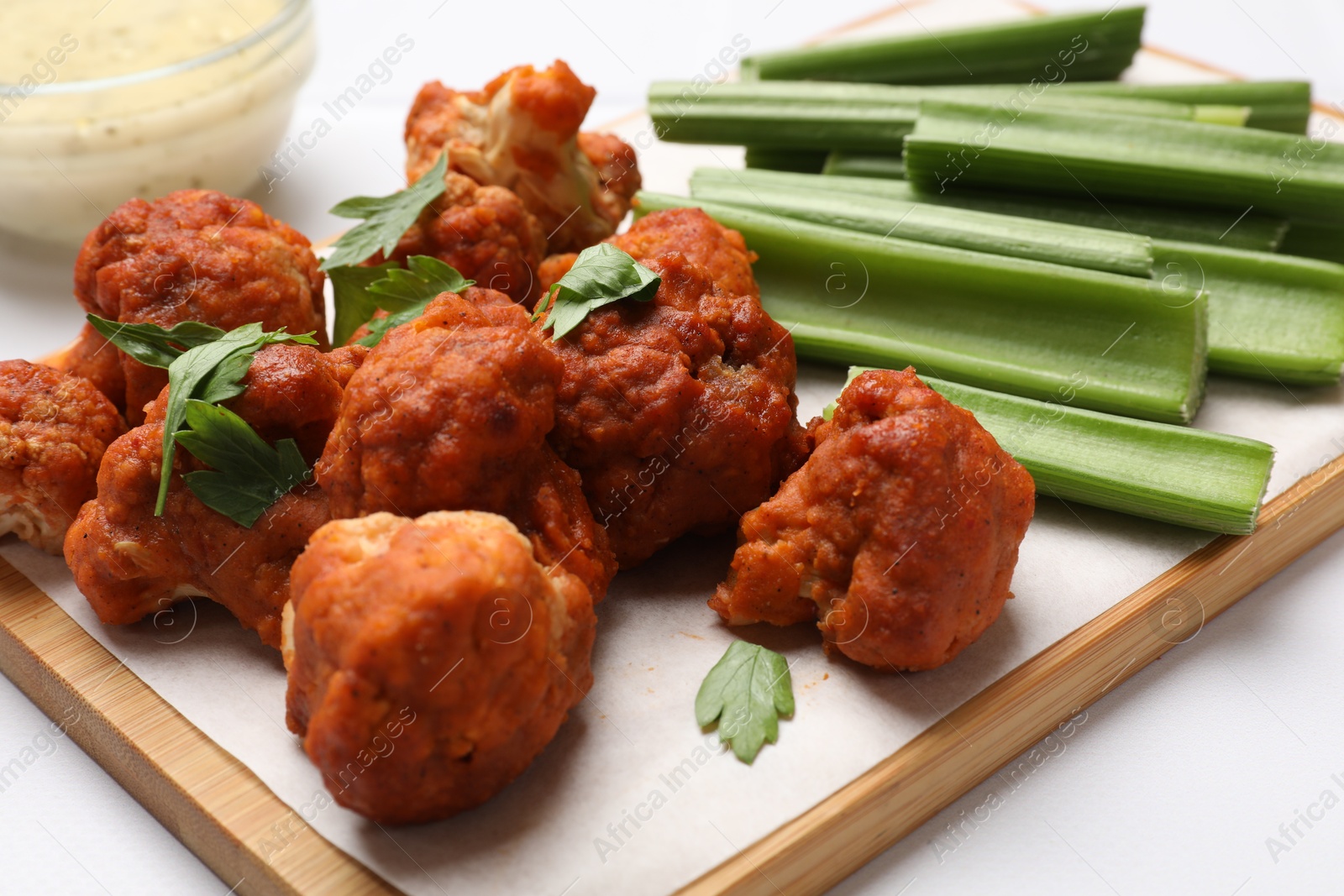 Photo of Baked cauliflower buffalo wings with parsley and celery on white table, closeup