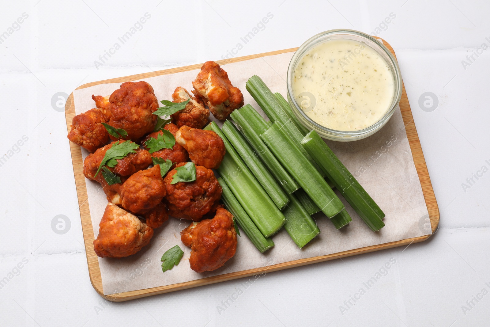 Photo of Baked cauliflower buffalo wings with celery and sauce on white tiled table, top view