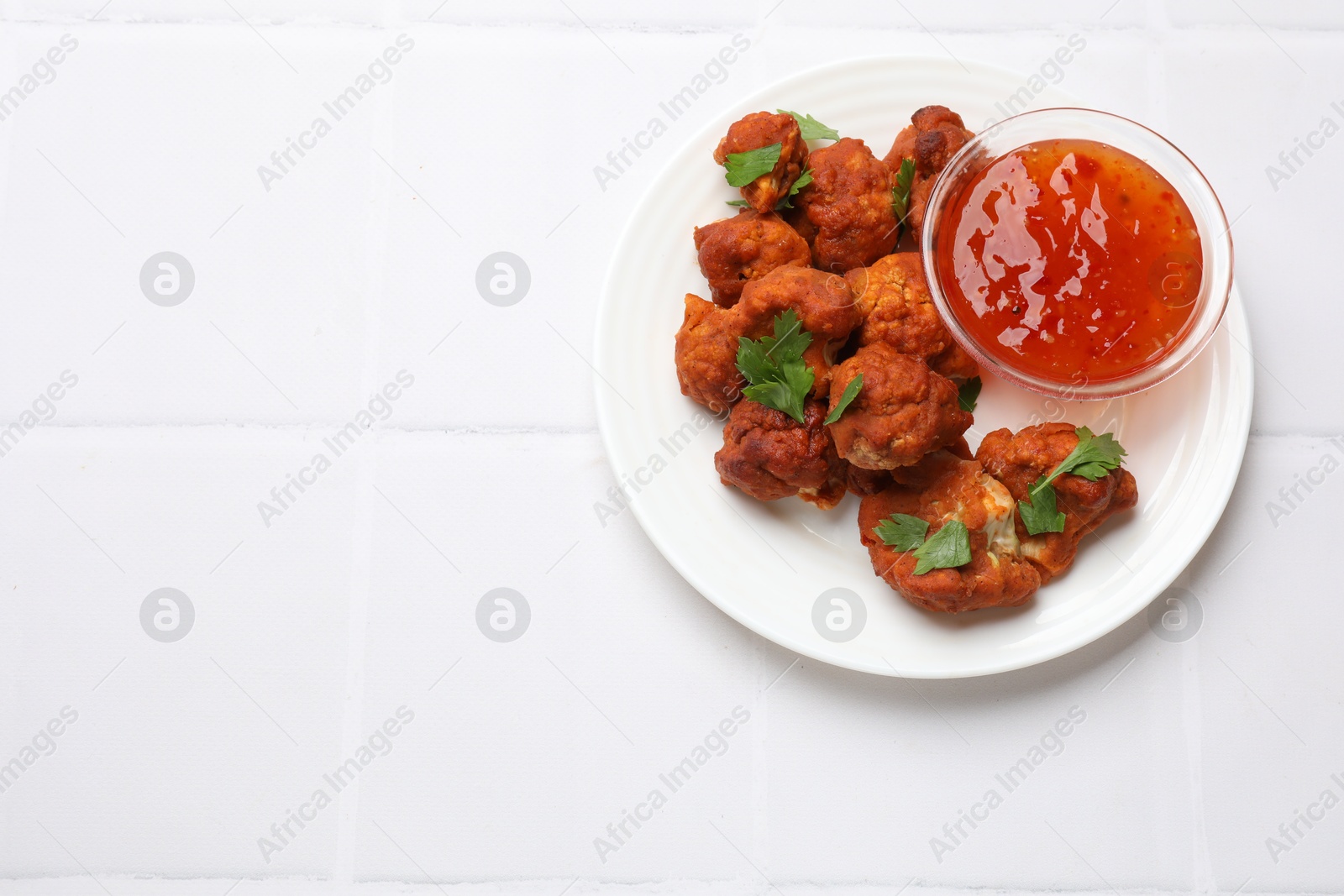 Photo of Baked cauliflower buffalo wings with parsley and sauce on white tiled table, top view. Space for text