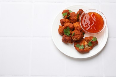 Photo of Baked cauliflower buffalo wings with parsley and sauce on white tiled table, top view. Space for text