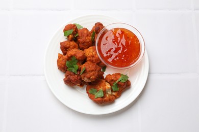 Photo of Baked cauliflower buffalo wings with parsley and sauce on white tiled table, top view