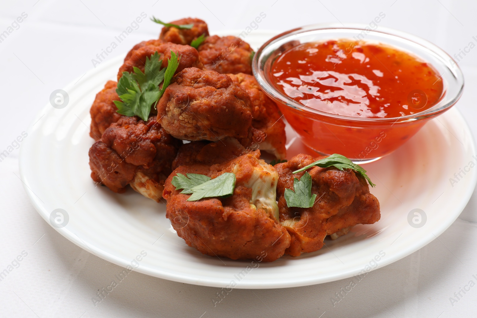 Photo of Baked cauliflower buffalo wings with parsley and sauce on white table, closeup