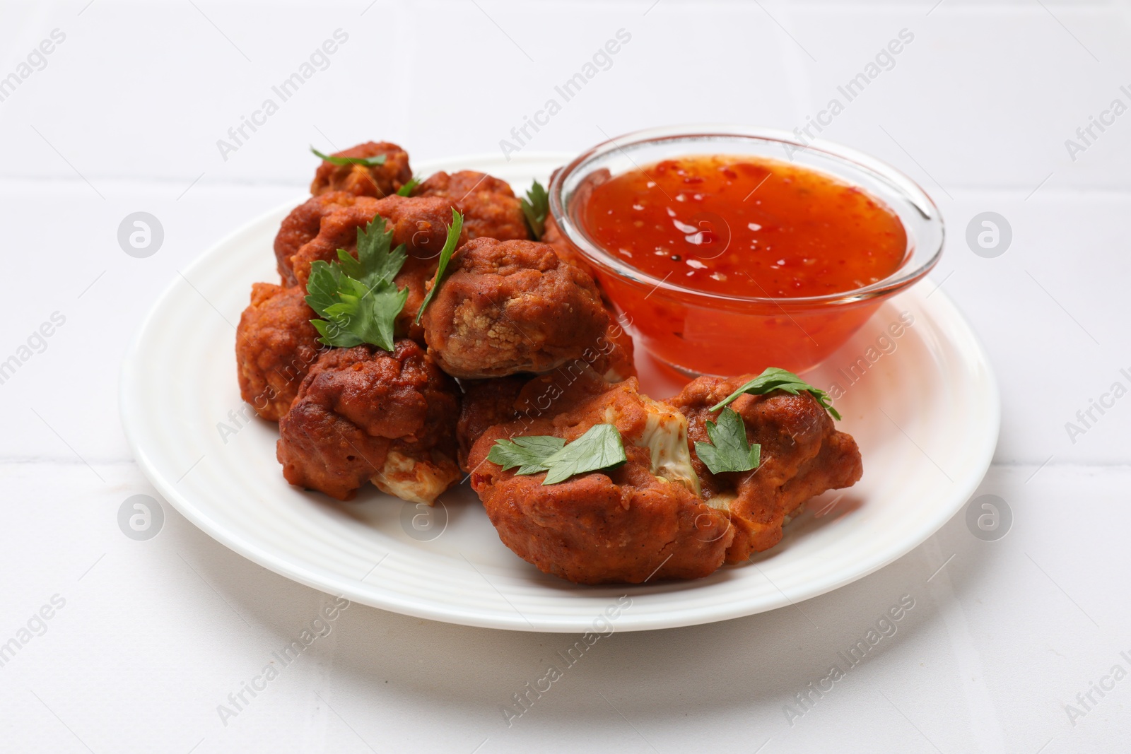 Photo of Baked cauliflower buffalo wings with parsley and sauce on white tiled table, closeup