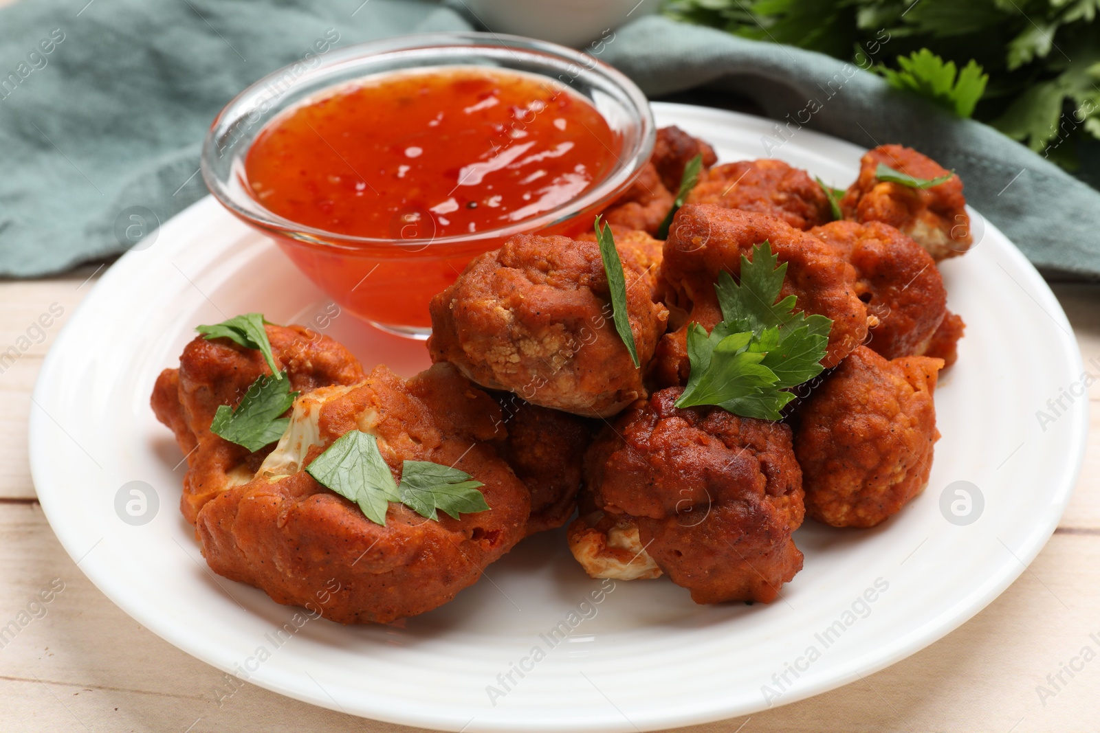 Photo of Baked cauliflower buffalo wings with parsley and sauce on wooden table, closeup