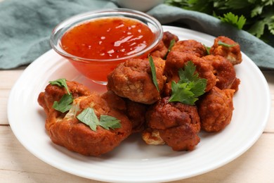 Photo of Baked cauliflower buffalo wings with parsley and sauce on wooden table, closeup