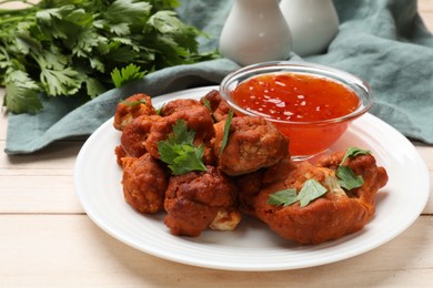 Photo of Baked cauliflower buffalo wings with parsley and sauce on wooden table, closeup