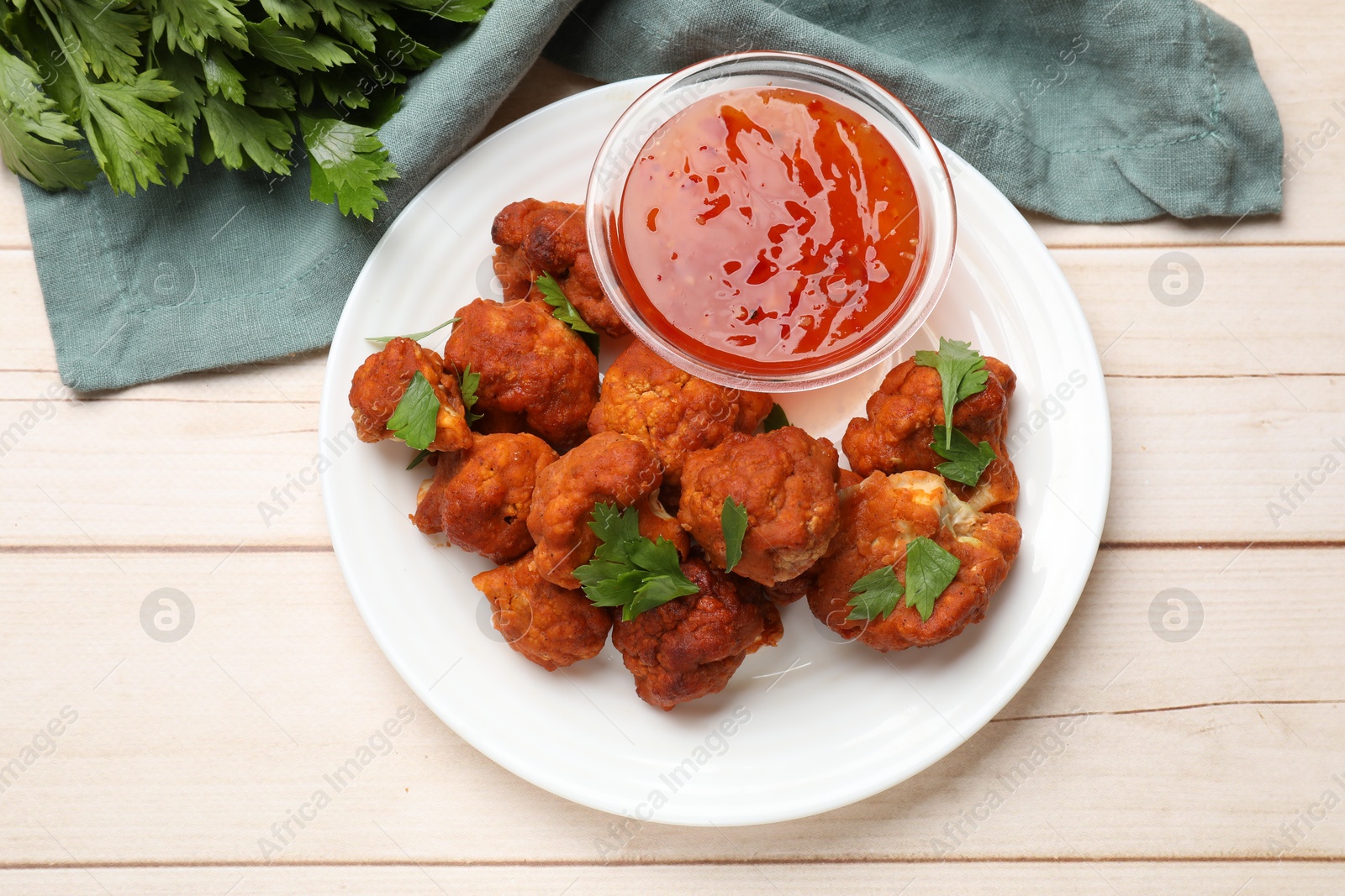 Photo of Baked cauliflower buffalo wings with parsley and sauce on wooden table, flat lay