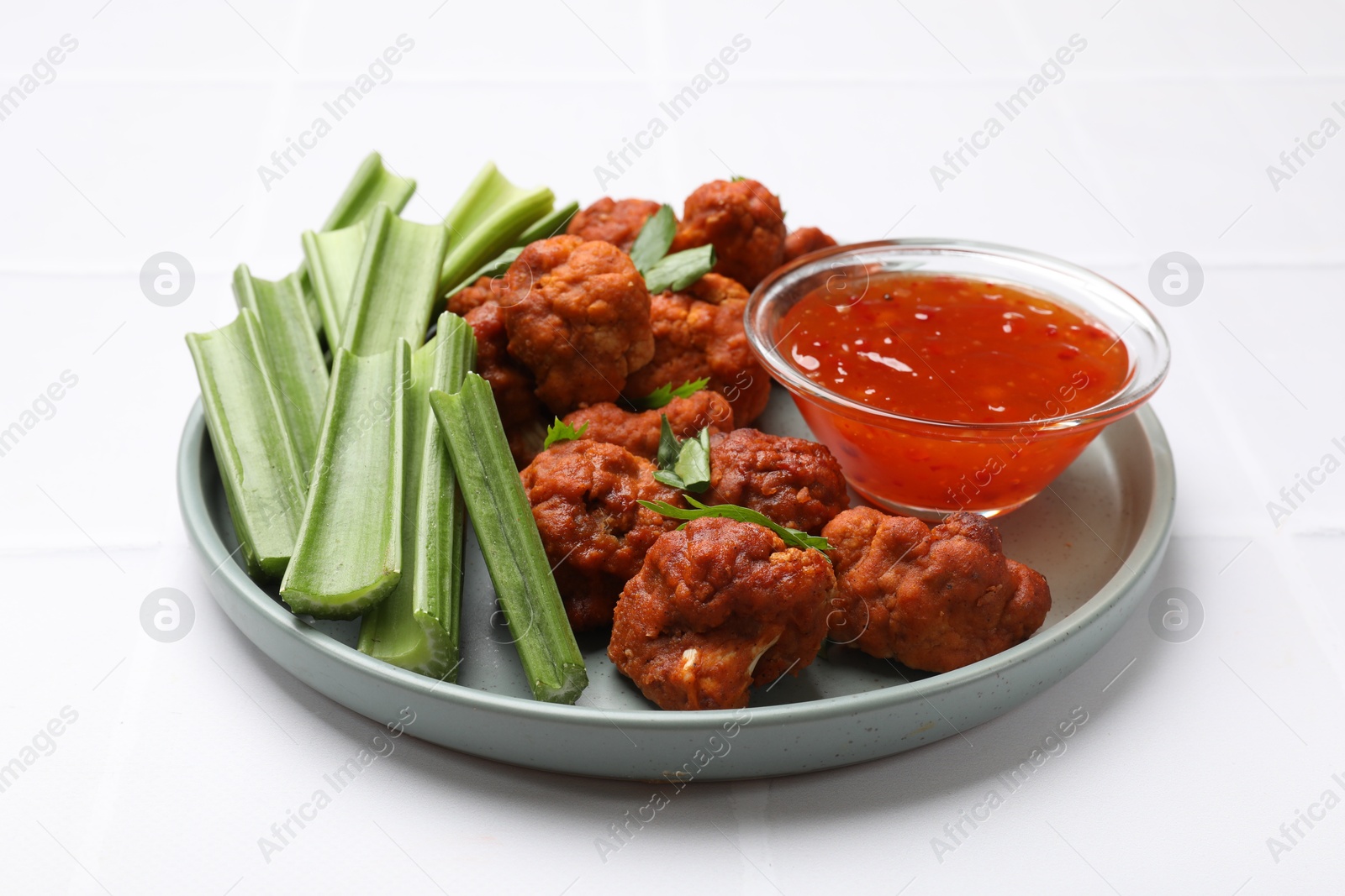 Photo of Baked cauliflower buffalo wings with celery and sauce on white tiled table, closeup