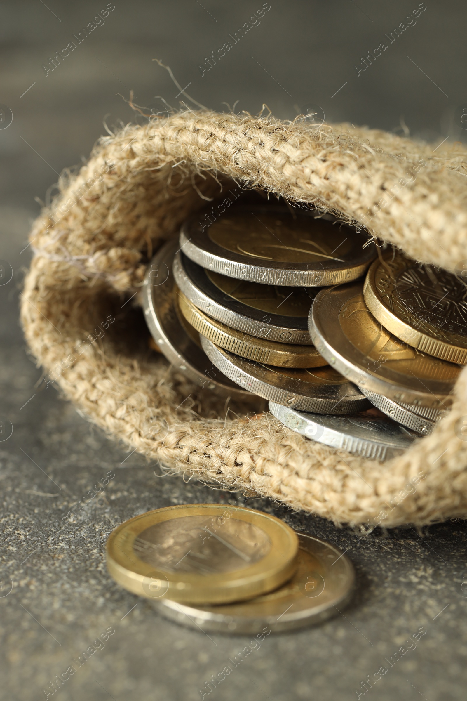 Photo of Euro coins in burlap sack on grey table, closeup