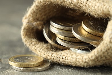 Euro coins in burlap sack on grey table, closeup