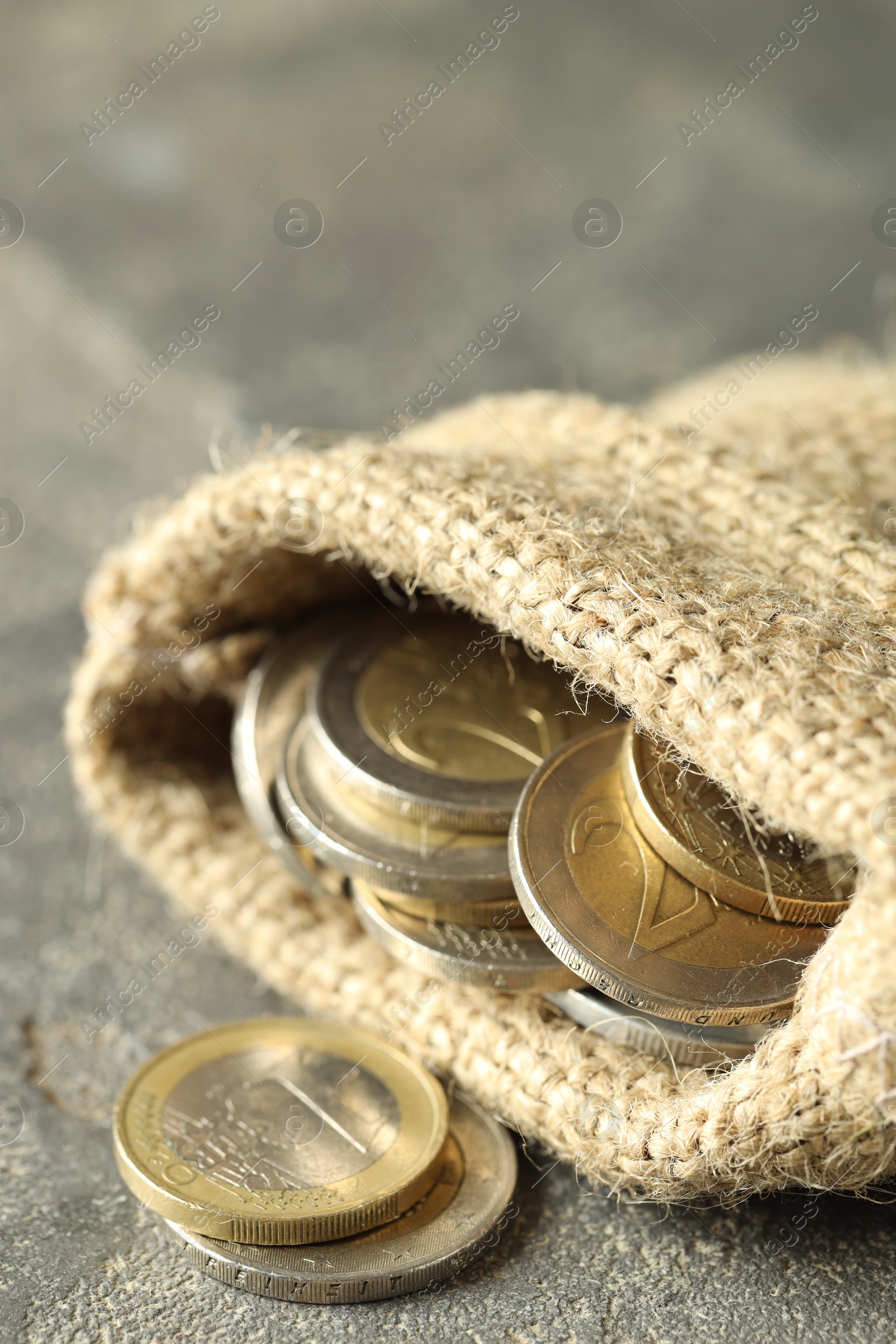 Photo of Euro coins in burlap sack on grey table, closeup