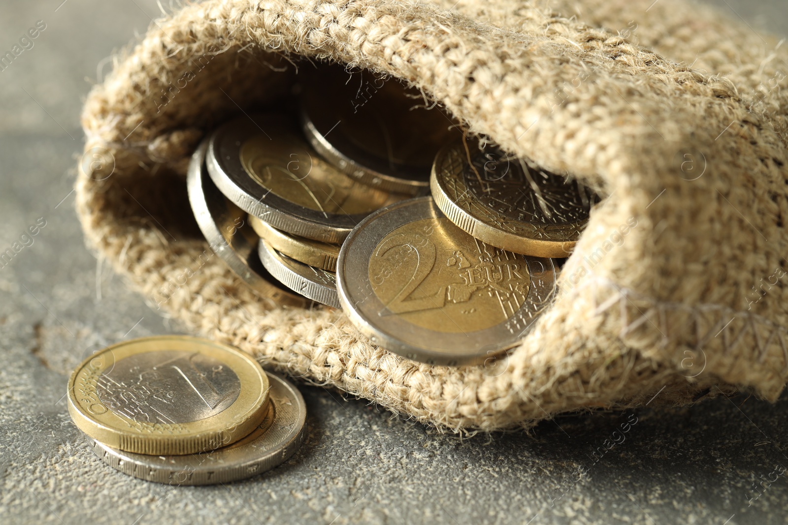 Photo of Euro coins in burlap sack on grey table, closeup