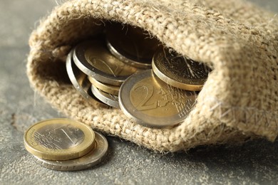 Euro coins in burlap sack on grey table, closeup