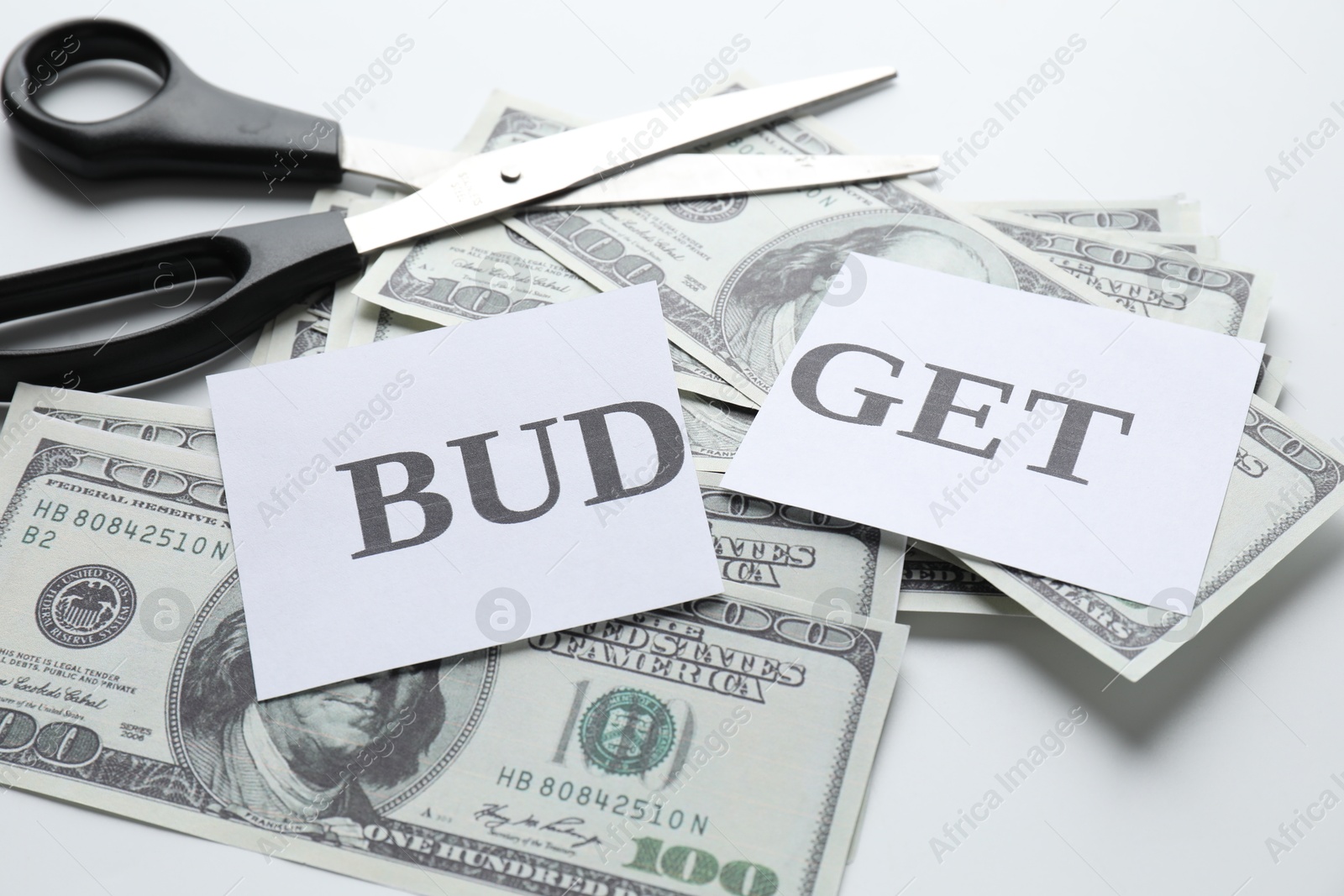 Photo of Cut paper with word Budget, dollar banknotes and scissors on white background, closeup