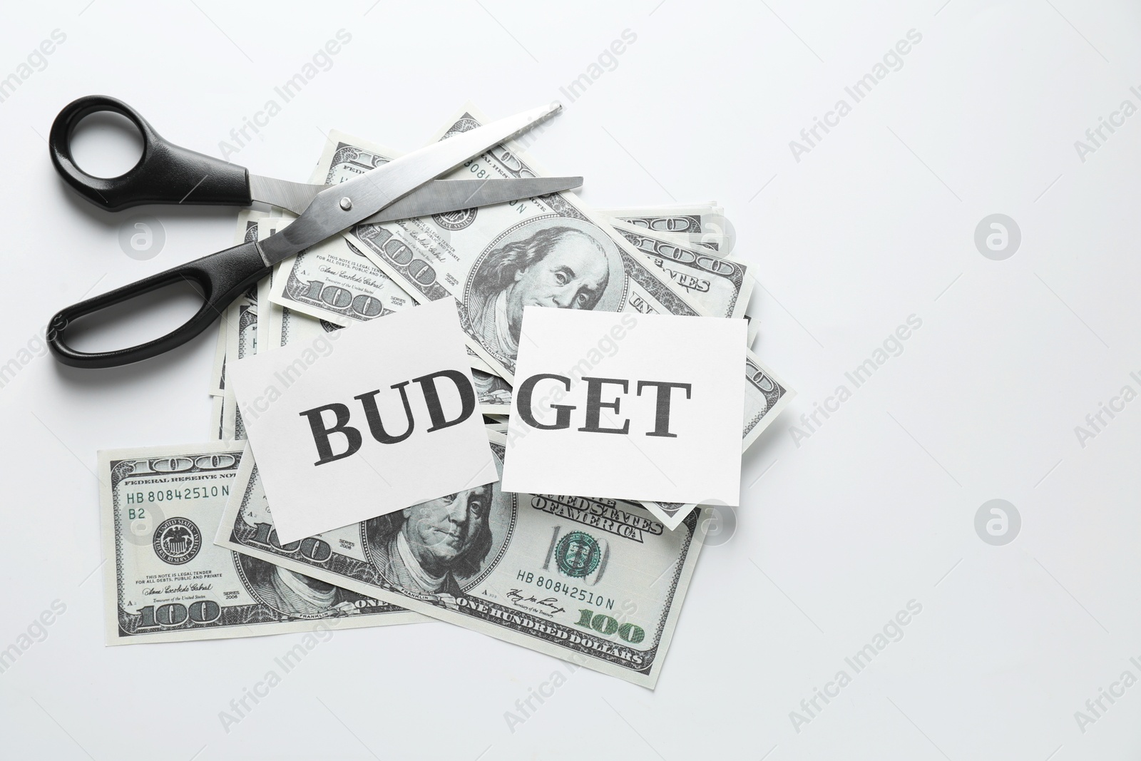 Photo of Cut paper with word Budget, dollar banknotes and scissors on white background, top view. Space for text