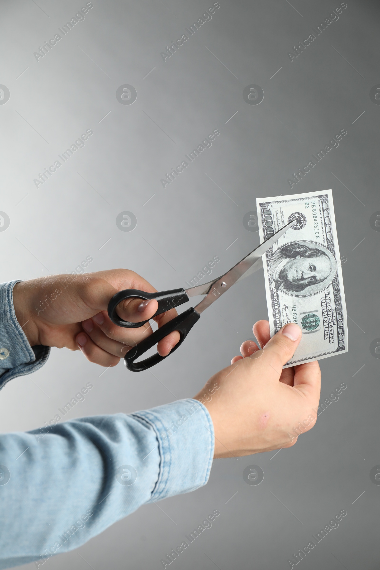 Photo of Budgeting. Man cutting dollar banknote with scissors on light grey background, closeup